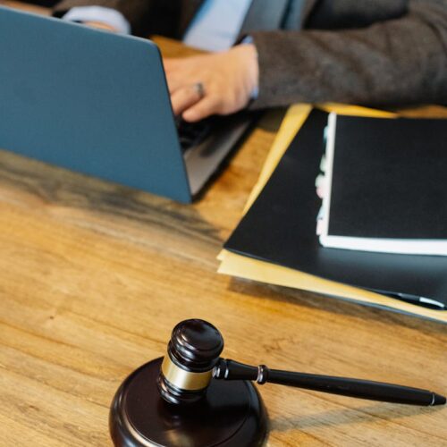 From above of crop anonymous male lawyer in formal clothes typing on laptop while sitting at wooden table with stack of documents and gavel